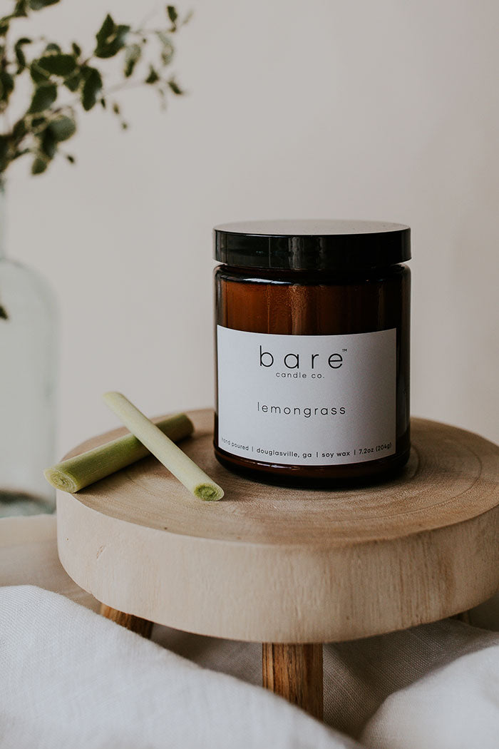 Lemongrass soy candle sitting on a platform with lemongrass sticks